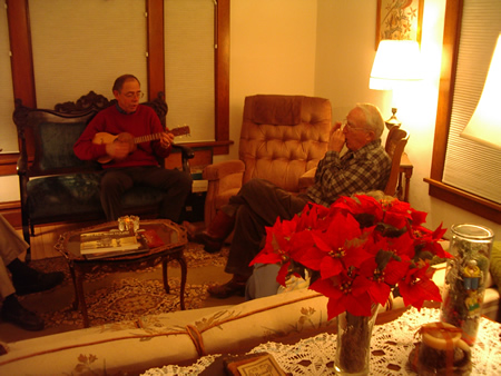 Photo of two people in a living room, one person paying ukulele